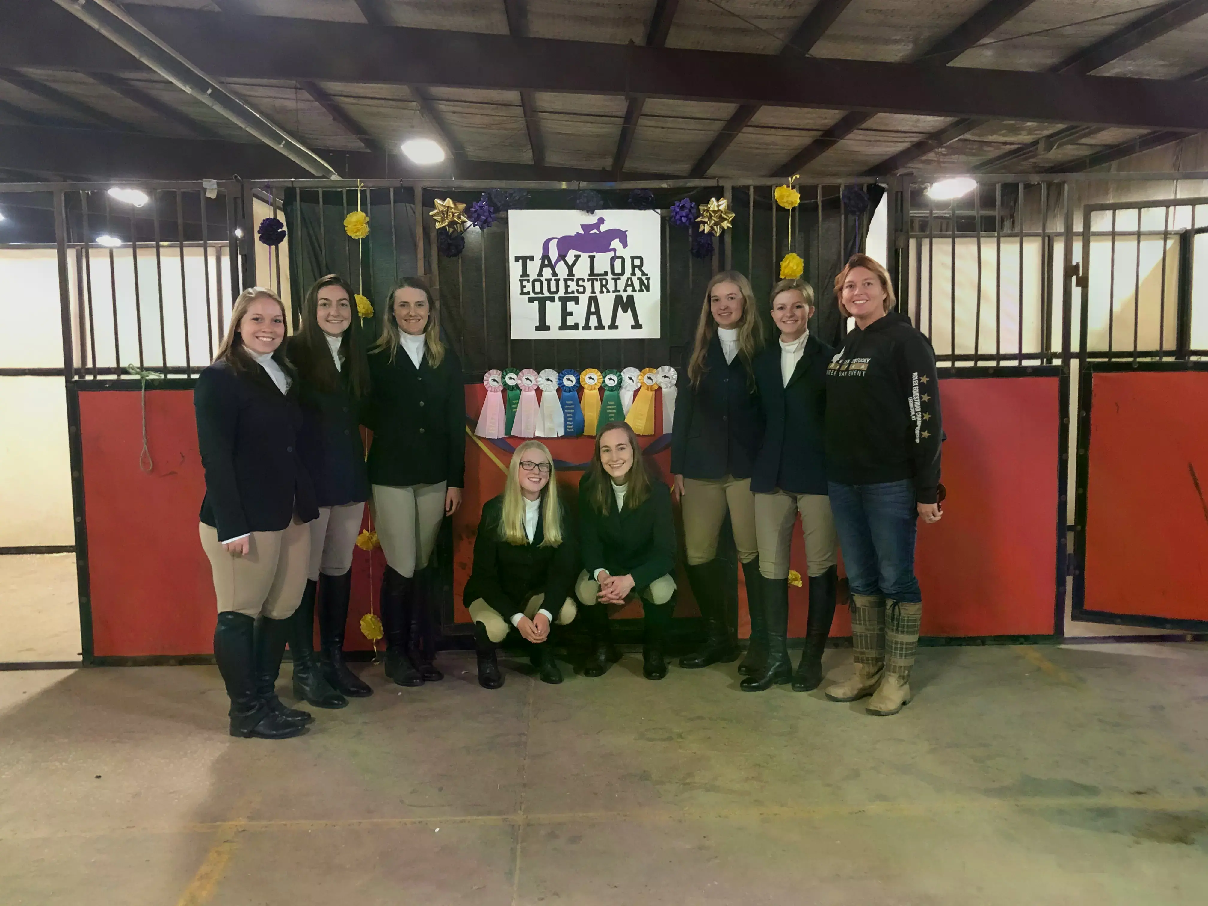 The Taylor Equestrian Team standing in the stable with all their ribbons